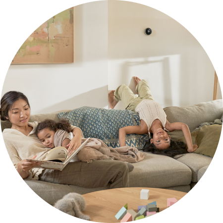 A mom and her two young daughters lay on the couch. The mom reads aloud to her kids.